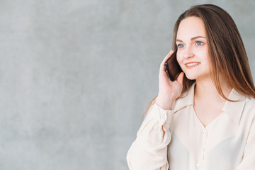 Business matters. Discussion and communication. Smiling beautiful woman talking on phone. Copy space on grey background.