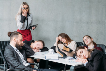 Tired corporate personnel. Overworking concept. Colleague looking at team members sleeping on desk...