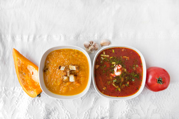 2 plates with red soup and pumpkin soup, vegetable soups, tomatoes, a piece of pumpkin clove of garlic on a white tablecloth, borsch, borscht