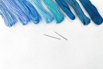 Flat lay top view with an embroidery canvas, needles, threads in blue colours