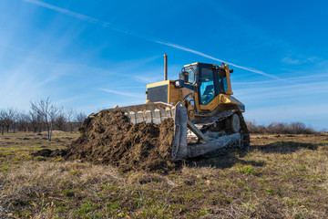 Obraz premium A big yellow bulldozer pushes the ground and makes a new road