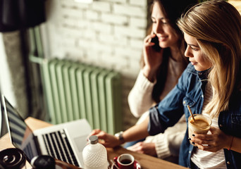 Young woman using laptop while enjoying in coffee time with her friend.
