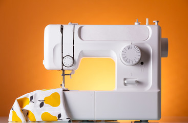 Modern white electric sewing machine with the fabric on bright yellow