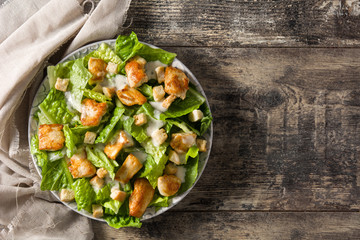 Caesar salad with lettuce,chicken and croutons on wooden table. Top view. Copyspace
