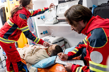 Paramedic writing in clipboard while colleague holding oxygen mask on patient