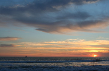 Naklejka na ściany i meble Lone sailboat crosses the horizon under a dramatic dusk sky