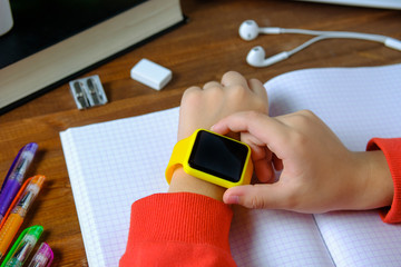 Little boy sitting at the table and looking smart watch. Smart watch for baby safety. The child...