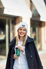 Young happy businesswoman with takeaway coffee standing on the street.