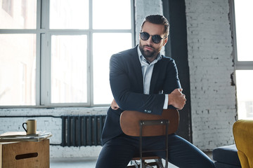 Young stylish businessman leader indoors at office wearing sunglasses looking aside thoughtful