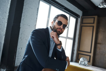 Young stylish businessman leader indoors at office wearing sunglasses looking aside thoughtful
