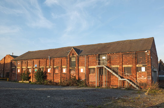 an old abandoned brick factory building with boarded up windows and steel staircase overgrown with weeds in leeds england