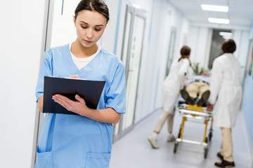 Concentrated nurse in blue uniform writing notes in clipboard