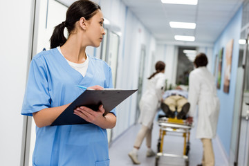 Brunette nurse in blue uniform writing notes in clipboard