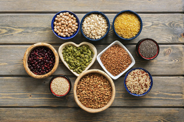 A set of various superfoods , whole grains,beans, seeds, legumes in bowls on a wooden plank table. Top view, copy space.