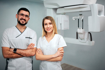 Two dentists stand in x-ray room and pose to camera. They smile and hold hands cossed....