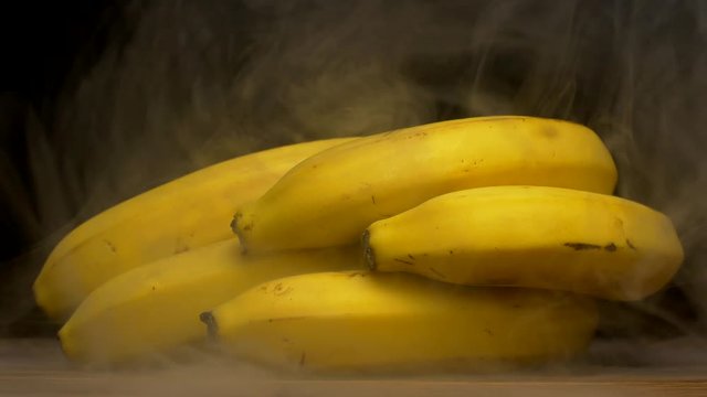 A bunch of fresh bananas on a black background from which comes sweat and cool, haze, close-up, 4K