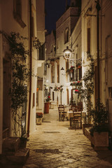 Fototapeta na wymiar Narrow white street and restaurant tables in Locorotondo, region Puglia, Italy