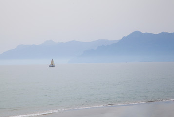 Fototapeta na wymiar View on Mediterranean sea from Salerno beach. A yacht alone in the evening on mountains background in fog.