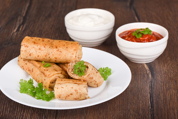Pancake rolls with meat filling, served with fresh parsley, sour cream and ketchup sauce