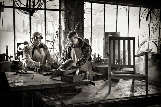 Two craftsmen in their craft workshops work metal parts 