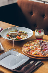 A fresh tasty pizza served with a glass of white wine on the wooden table in the restaurant