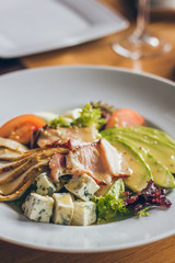 Tasty fresh salad with different ingredients like salad, tomatoes, meat, cheese in the restaurant on the white plate