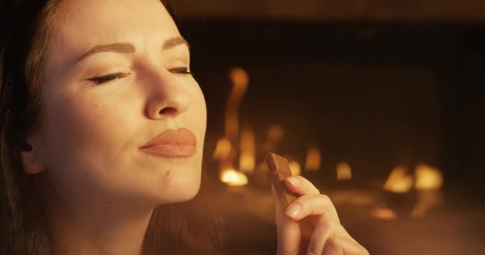 Attractive Female Bitting Chocolate Dessert Closing Eyes Delighting in the Taste Indoors at Fireplace 