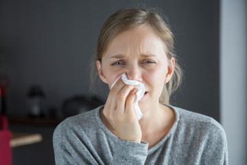Unhappy sick woman blowing nose with napkin, looking at camera