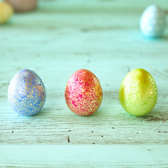 Three colorful Easter eggs on green wood