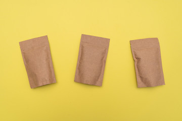 Three identical packages on a zipper made of brown paper with unknown contents and empty space on the front side, arranged in a row on a yellow background