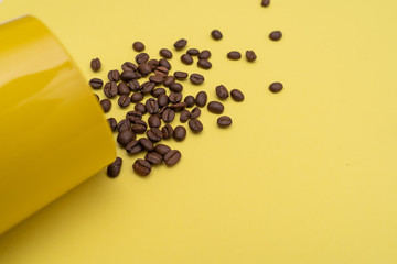 Roasted coffee beans scattered from yellow aluminum can on a yellow surface
