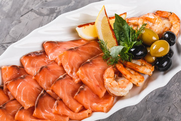 Seafood platter with salmon slice, shrimp, slices fish fillet, decorated with olives and lemon in plate over rustic background. Mediterranean appetizers