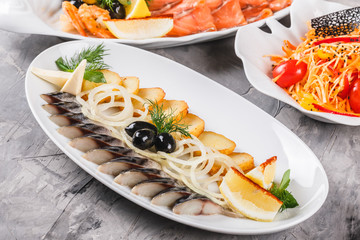 Seafood platter with smoked mackerel slice, fried potatoes, slices fish fillet, decorated with onion and lemon in plate over rustic background. Mediterranean appetizers. Top view