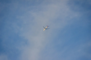 Faraway flying airplane against blue sky and white cloud background.