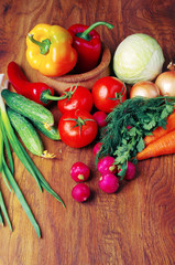 Appetizing vegetables on a wooden table. Tomatoes, cucumbers, radishes, carrots, peppers, parsley.