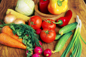 Appetizing vegetables on a wooden table. Tomatoes, cucumbers, radishes, carrots, peppers, parsley.