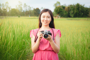 Portrait of the Asian pretty girl in vintage pink dress holding a film camera in the meadow.