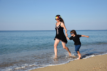 Mother and son playing on the beach. Mom and child holding hands and running to the sea