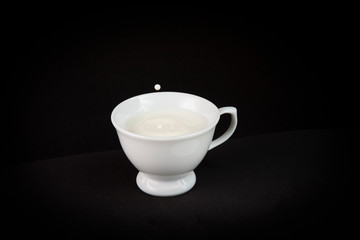 Tiny coffee cup filled with milk with a splash creating a drop of milk floating in mid air above the cup