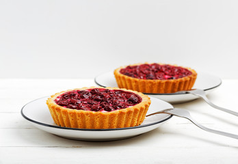 Tasty homemade cherry cheese tartlets on white wooden table. Front view against white background. Copyspace.