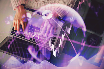 Hands typing on laptop. Business and Financial concept. Double exposure of stock market charts.