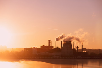 View of factory pipes emitting pollution into the atmosphere. Environmental problems. Sunset red sun