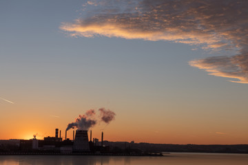 View of factory pipes emitting pollution into the atmosphere. Environmental problems. Sunset red sun
