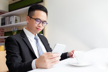 Portrait of smart and handsome Asian business man using a smartphone on coffee bar in the coffee shop close up.