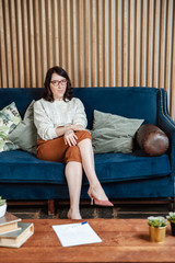 Obraz premium A young girl in a light jacket and brown trousers stands on a blue sofa, and a low table with books in the front.