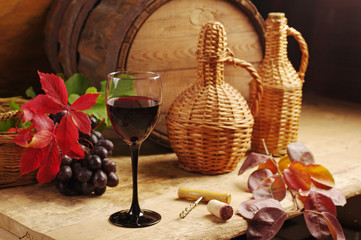 A glass of wine, a bottle, grapes on the background of a wine barrel.