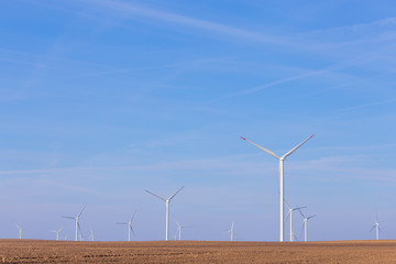 Farm of windmill turbines on agricultural field with blue sky in background. Renewable energy wind...