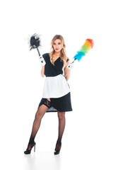 attractive housemaid in black uniform, apron and stockings standing with multicolored broom on white background