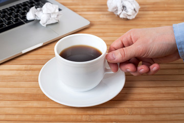 man holding cup of hot beverage, laptop on wooden table, close up