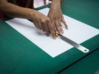 Close-up hands cutting white paper with cutter and iron ruler on green mat